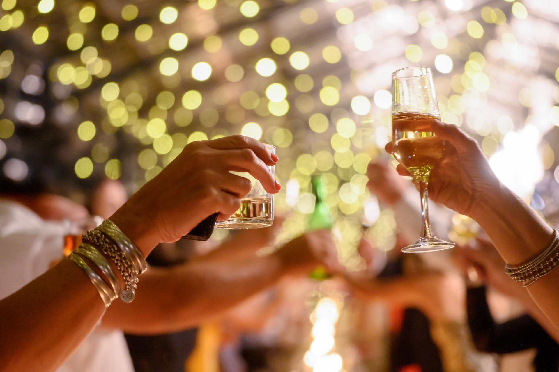 Célébration festive mettant en vedette des mains levant des boissons avec une chaîne dorée fond bokeh clair